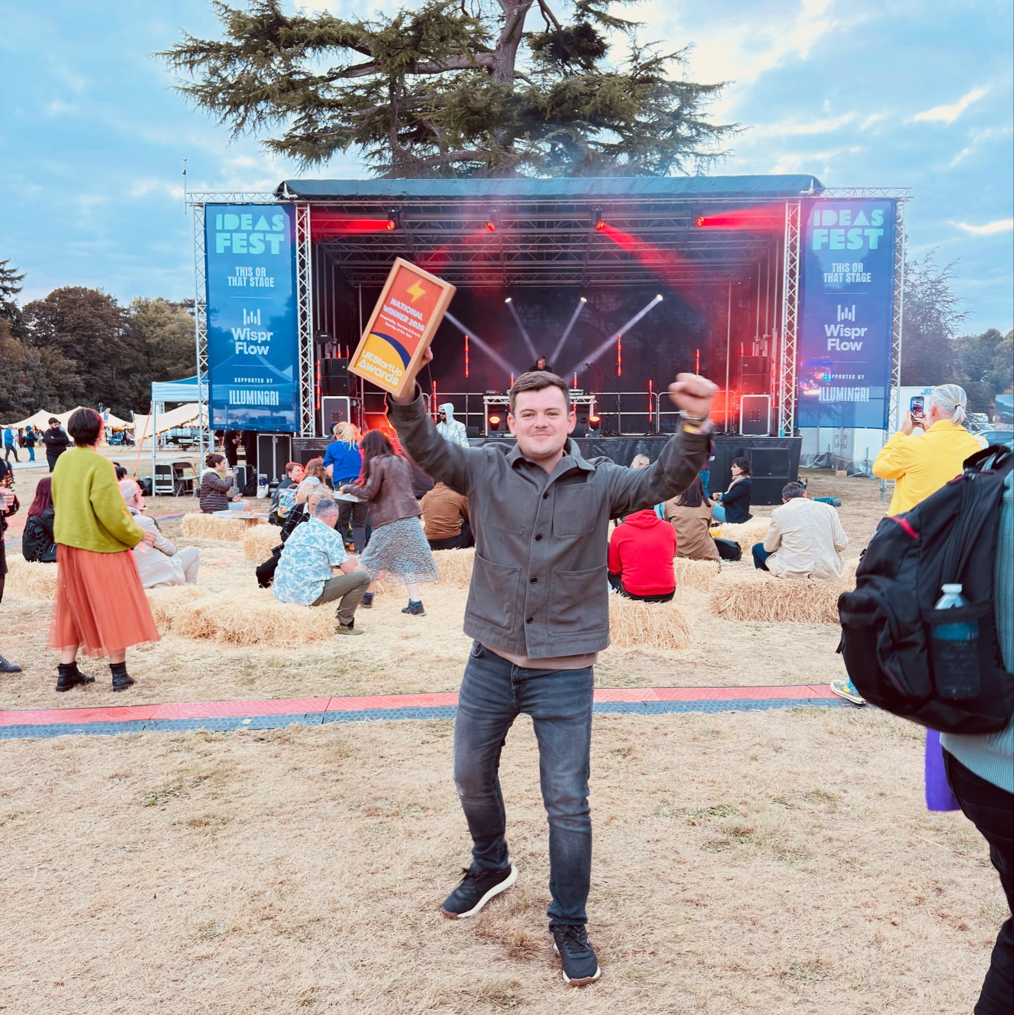 Dion Wright raising Booking Hub's national winner trophy from the UK StartUp Awards in front of the Ideas Fest stage.